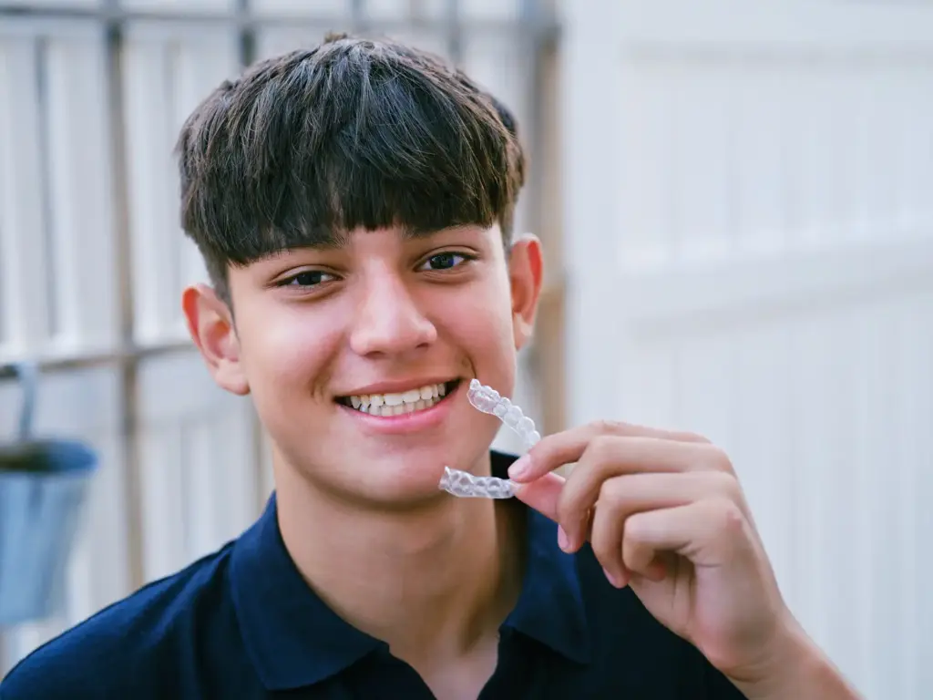 Adolescent somrient mentre mostra el seu aparell d'ortodòncia invisible Invisalign.